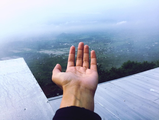 Foto beschnittene hand einer person über der landschaft gegen den himmel