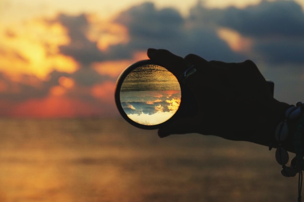 Foto beschnittene hand hält eine kristallkugel gegen den himmel bei sonnenuntergang