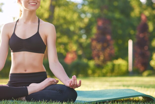 Beschnittene horizontale Aufnahme einer jungen Frau, die freudig Yoga beim Park Copyspace Glück Harmonie Balance Asana Konzept lächelt.