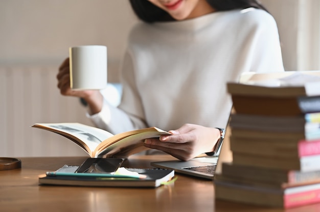 Beschnittene Schussfrau, die Kaffeetasse beim Lesen des Buches hält.