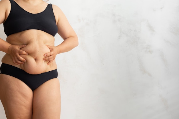 Beschnittene übergewichtige Frauen in schwarzen Dessous, die den baumelnden Bauch berühren und zusammendrücken Fette Cellulite-Nahrungsmittelsucht überessen