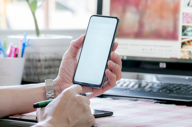 Beschnittener Schuss der Mannhand, die Smartphone mit leerem Bildschirm beim Sitzen und Arbeiten im modernen Büro hält.