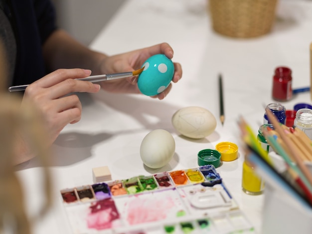 Beschnittener Schuss der weiblichen Handmalerei auf Ei, das für Osternfest zu Hause vorbereitet