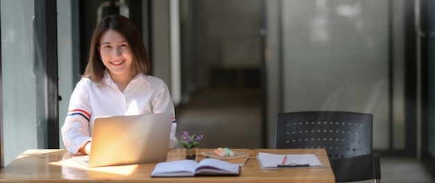 Beschnittener Schuss des glücklichen Universitätsstudenten, der am Laptop arbeitet