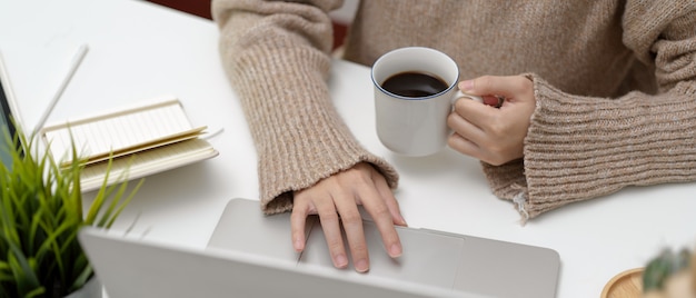 Beschnittener Schuss des Studenten, der Laptop verwendet, während Kaffee hochhält