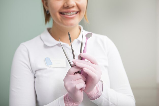 Beschnittener Schuss einer Zahnärztin mit lächelnden Zahnspangen, die zahnärztliche Werkzeuge halten