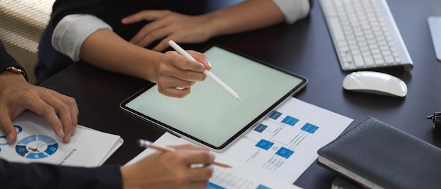 Beschnittener Schuss von Geschäftsmannhänden, die mit Tablette und Geschäftskarte auf dem Tisch arbeiten