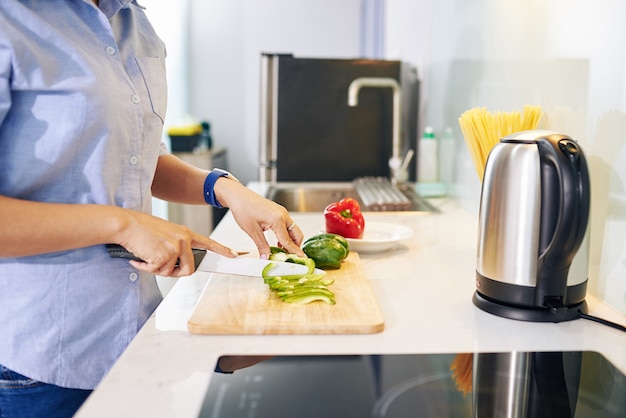 Beschnittenes Bild der Hausfrau, die am Küchentisch steht und Paprika für gesunden Salat schneidet