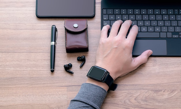 Beschnittenes Bild der Mannhand, die Smartwatch trägt, die auf Tabletttastatur, Draufsicht, Kopienraum arbeitet.