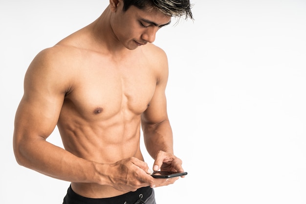 Beschnittenes Bild des asiatischen jungen Mannes mit dem muskulösen Körper, der ein Smartphone mit zwei Handschreibständern hält, die nach vorne schauen und ein Telefon betrachten