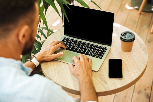 Beschnittenes Bild des jungen bärtigen Mannes unter Verwendung des Laptops