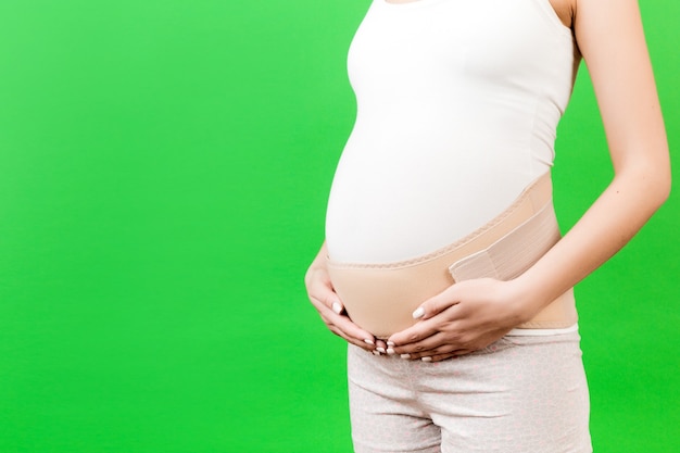 Beschnittenes Bild des unterstützenden Verbandes auf der schwangeren Frau an der grünen Oberfläche mit Kopienraum