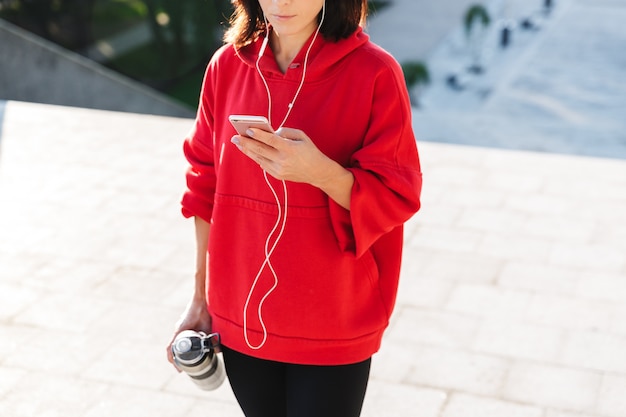 Beschnittenes Bild einer jungen Sportlerin, die Musik mit Kopfhörern hört, während sie sich nach dem Training ausruht