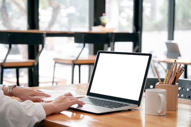 Beschnittenes Bild von Frauenhänden, die auf Laptop-Computer arbeiten, während sie am Tisch sitzen.