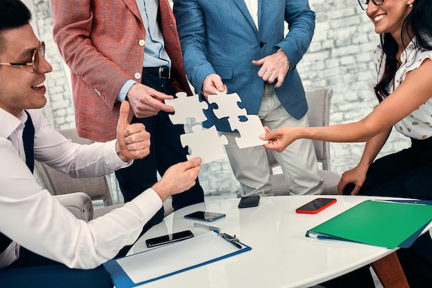 Beschnittenes Bild von Geschäftsleuten, die Puzzleteile im Büro verbinden