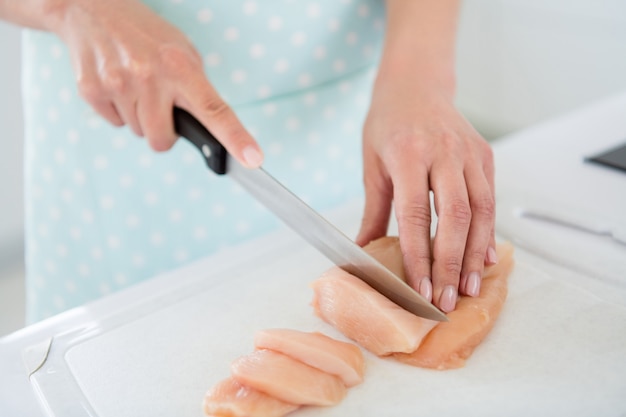 Beschnittenes Nahaufnahmefoto von Hausfrauenhänden, die Hühnerfleischwochenende schneiden, das leckere Zubereitung des Abendessens kocht, warten Familie zu Hause weißes Licht Küche drinnen