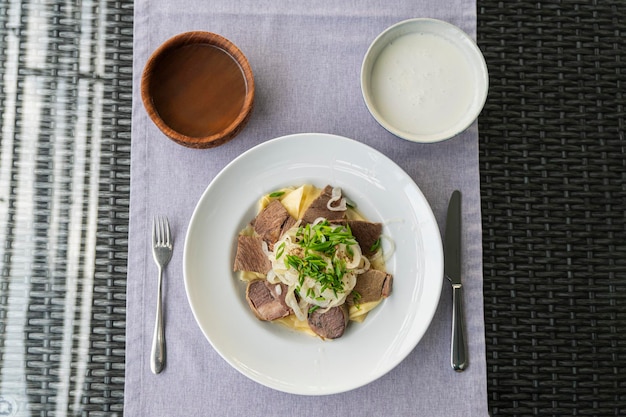 Beshbarmak plato nacional kazajo preparado con carne y pasta Plato Beshbarmak primer plano en un plato sobre la mesa Grandes trozos de carne guisada y cebolla