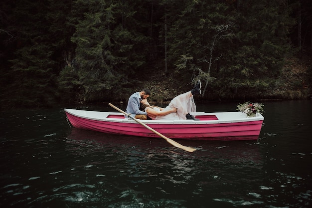 Beso de boda en el barco retro. Novios sentados en barco rosa flotando en el lago.