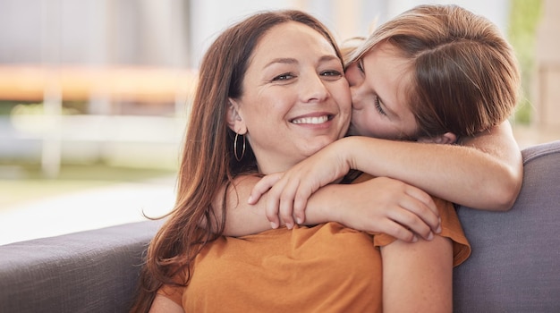 Beso familiar y niña con madre en un sofá para abrazar amor y dulce momento en una sala de estar juntos Retrato feliz familia y mamá con hija en un sofá abrazar y disfrutar de tiempo de calidad en casa