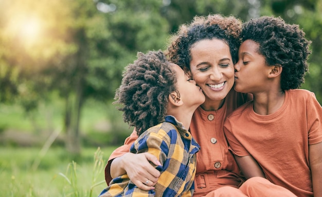 Beso feliz y madre con niños en el parque para relajarse, vincularse y amar la maqueta, apoyo de atención y sonrisa con mujeres y niños en el campo de hierba en la naturaleza para el verano familiar negro y la felicidad juntos