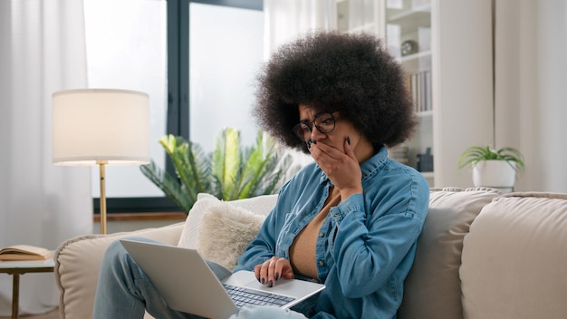 Besorgte afroamerikanische Frau, gestresst mit Laptop, frustriert, verzweifelt, schockiert, traurig, verärgert, schlecht lesen