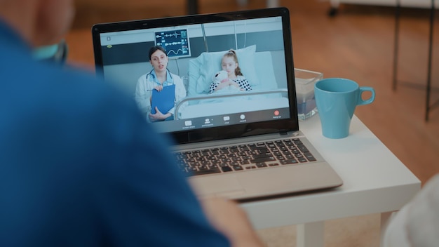 Besorgte Großeltern nutzen Videokonferenzen auf dem Laptop, um mit Sanitätern und kleinen Mädchen im Krankenhaus zu sprechen. Rentner, die zur Kommunikation an Online-Telekonferenzen auf dem Computer teilnehmen.