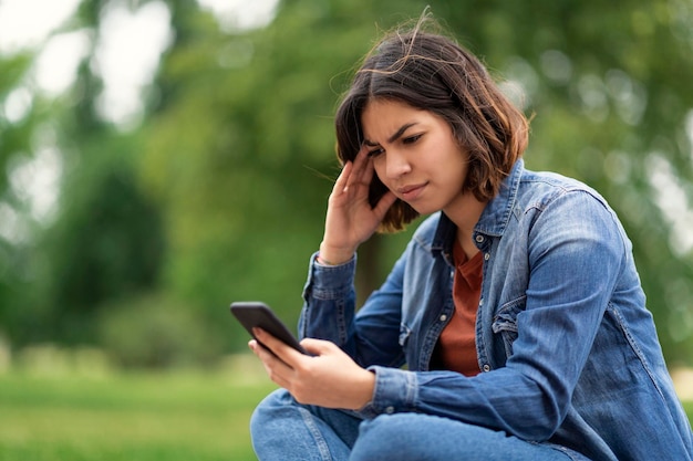 Besorgte junge arabische Frau, die eine Nachricht auf dem Smartphone liest, während sie im Freien sitzt