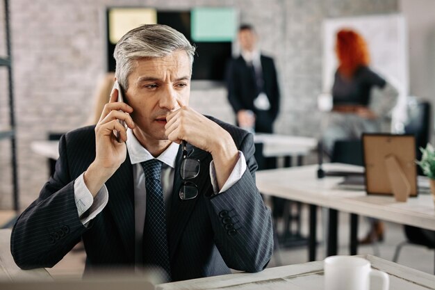 Besorgter Geschäftsmann, der beim Telefonieren über das Handy im Büro nachdenkt