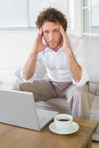 Besorgter gut gekleideter Mann, der zu Hause mit Laptop sitzt