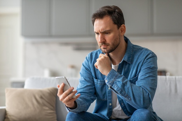 Besorgter Mann liest zu Hause auf der Couch auf dem Smartphone