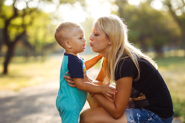 Besos y abrazos de mamá e hijo. Mamá e hijo caminan por el parque de verano.