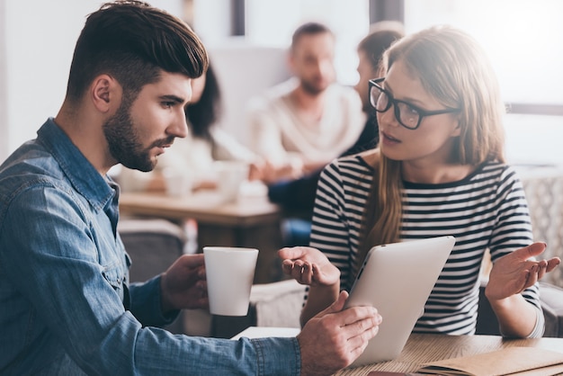 Besprechen der Arbeit. Junge schöne Frau, die ihren Kollegen beim Sitzen am Bürotisch gestikuliert und anschaut