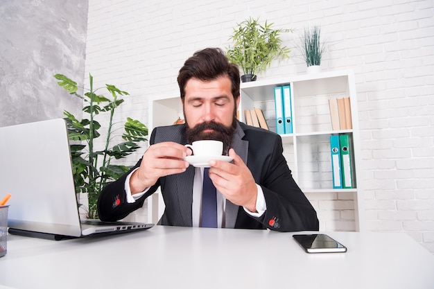 Besprechen Sie das Geschäft beim Kaffee. Respektabler Geschäftsführer. Der gutaussehende Chef des Mannes sitzt im Büro und trinkt Kaffee. Bequemer Arbeitsplatz. Guten Morgen. Bärtiger Hipster-Anzug, der sich mit Kaffee entspannt. Routinen im Büroalltag.