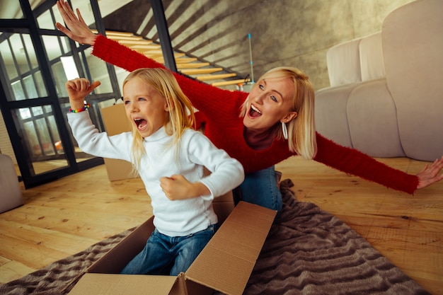 Besser zusammen. Fröhliches blondes Mädchen, das den Mund öffnet, während es in einer Pappschachtel sitzt