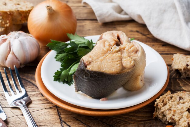 Bestandteile für Lachsfischsuppe, Stücke Brot, Zwiebel und Knoblauch mit Grüns auf Holztisch.