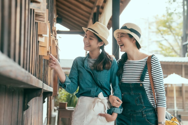 beste freunde genießen die gemeinsame zeit und besuchen die alte stadt in kyoto, japan. Glückliche zwei Schwestern, die im Gehweg im Freien spazieren gehen und ein Holzbrett berühren, das am Fenster hängt. Frauen lesen Wünsche.