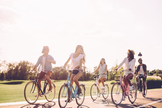 Beste Freunde und Weg voraus. Gruppe junger Leute, die Fahrrad entlang einer Straße fahren und glücklich aussehen