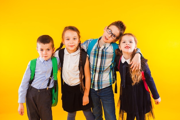 Beste Schulfreunde, die sich zusammen umarmen Glücklich lächelnde Klassenkameraden, die an der gelben Wand stehen Schulkinder, die Freundschaft genießen