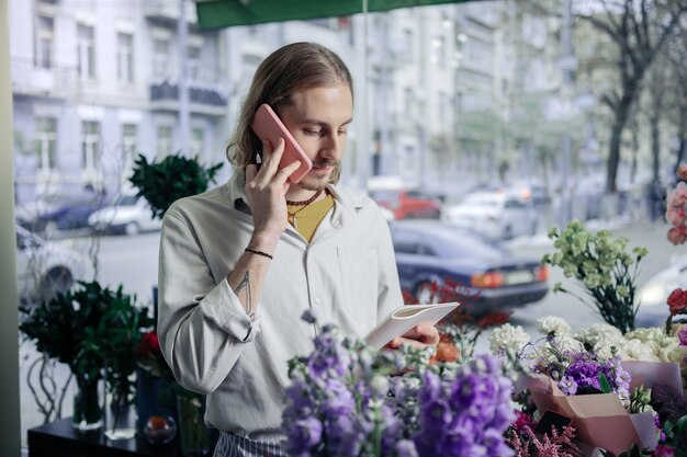 Bestellung ist beendet. Ernsthafter Florist, der pro Telefon spricht, während er Liste der Blumen liest