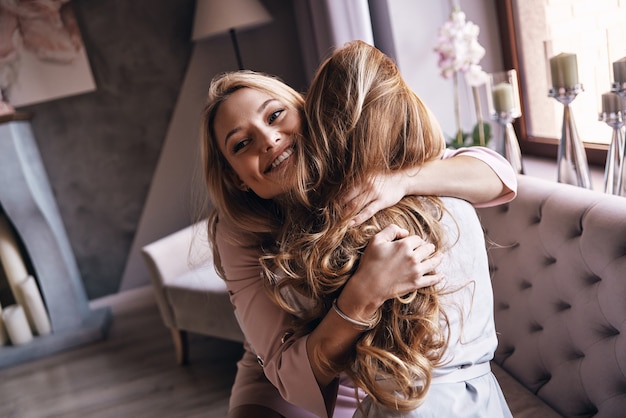 Besten Freunde. Draufsicht auf attraktive junge Frauen in eleganten Kleidern, die sich beim Sitzen auf dem Sofa umarmen und lächeln