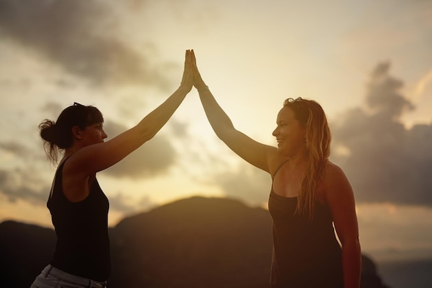 Bester Urlaub aller Zeiten Aufnahme von zwei glücklichen jungen Freunden, die sich bei Sonnenuntergang gegenseitig High-Five geben