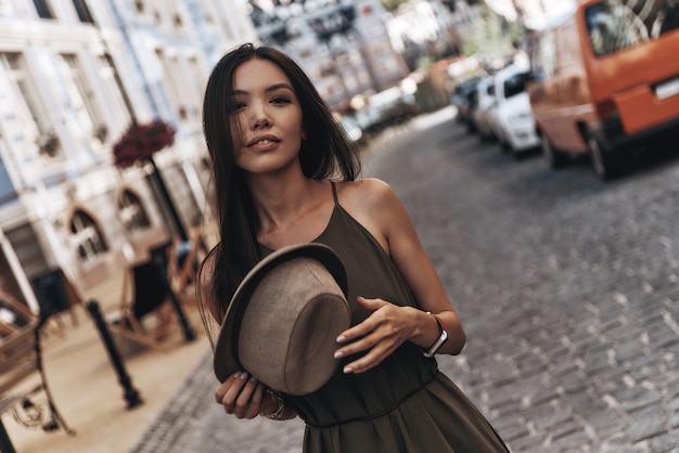 Bestes Sommer-Accessoire. Attraktive junge Frau, die ihren Hut hält, während sie im Freien steht