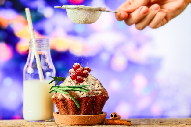 Bestreuen Sie den Kuchen mit Puderzucker Cupcake auf dem Hintergrund eines Weihnachtsbaums mit Milch