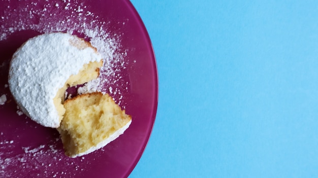 Bestreuen Sie einen Hüttenkäse mit Puderzucker auf einem rosa Teller auf blauem Hintergrund, Draufsicht. Dessert, ein kleiner Cupcake. Lebensmittelkonzept. weiße gebackene Kekse mit einer luftigen Textur. Platz kopieren.