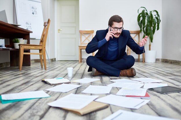 Betonter Geschäftsmann, der an Boden im Büro arbeitet