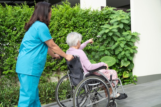 Betreuer helfen und pflegen eine ältere asiatische Patientin, die im Rollstuhl auf der Rampe im Krankenhaus sitzt