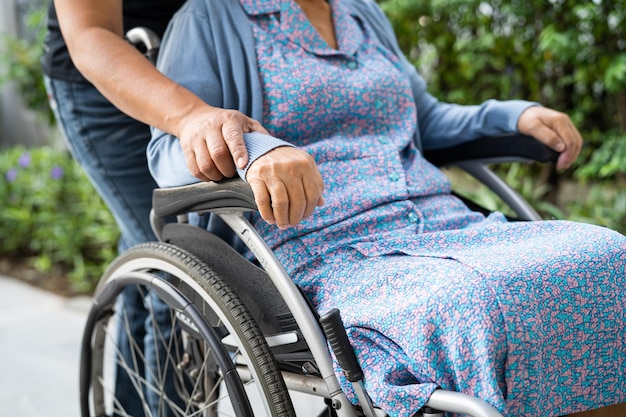 Betreuer helfen und pflegen eine asiatische ältere Patientin, die im Rollstuhl auf der Rampe im Pflegekrankenhaus sitzt, gesundes, starkes medizinisches Konzept