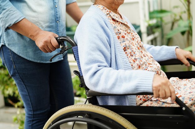 Betreuerin hilft einer asiatischen älteren Frau mit Behinderung, die im Krankenhaus im Rollstuhl sitzt