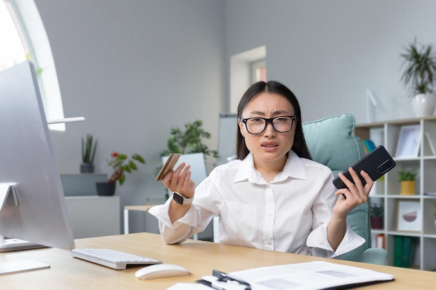 Betrug verärgerte junge schöne asiatin, die telefon und kreditkarte hielt, eine enttäuschte junge dame verlor