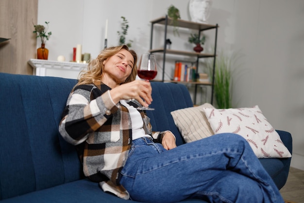 Betrunkene Frau mittleren Alters mit einem Glas Rotwein auf dem Sofa zu Hause